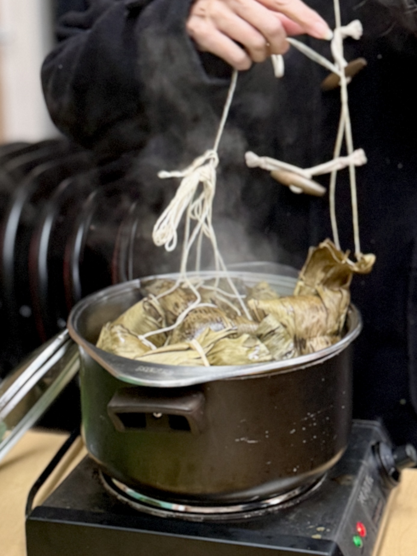 Steaming pot of wrapped rice parcels being lifted out with twine