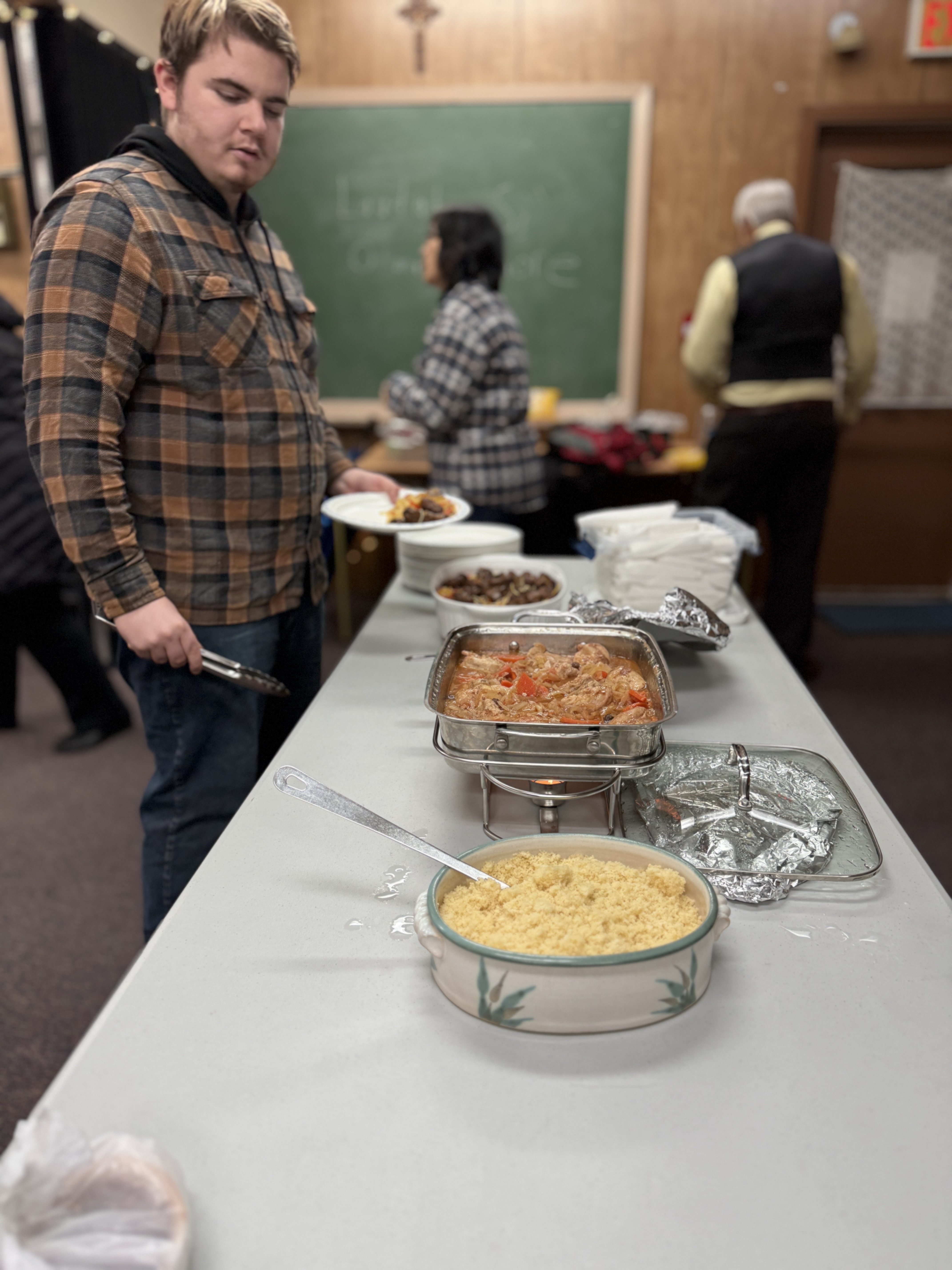 Serving table with warm dishes and parishioners filling their plates